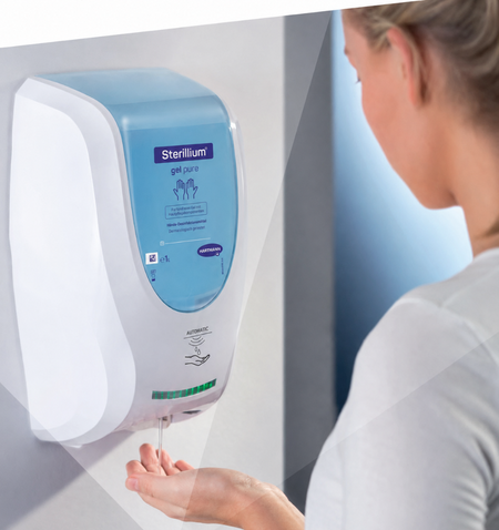 Frau hält die Hand unter einen automatischen Sterillium Gel Pure Spender zur berührungslosen Händedesinfektion.