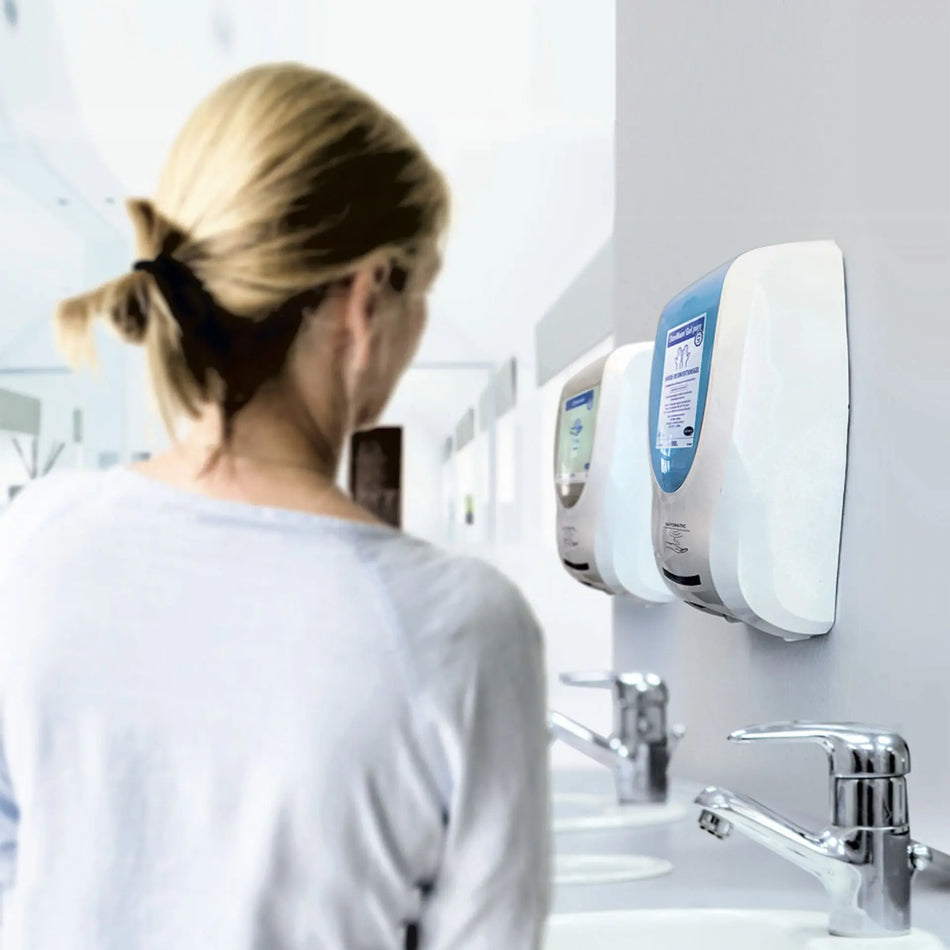 Weißer Desinfektionsmittelspender mit einem sensorgesteuerten Ausgabemechanismus, montiert an einer Wand. Der Spender hat eine klare, transparente Front zur Sichtbarkeit des Inhalts und eine schlichte, moderne Form. Auf der oberen Fläche befindet sich ein silbernes Bedienfeld. Der Hintergrund ist hell und neutral gehalten, wodurch der Spender hervorsticht.