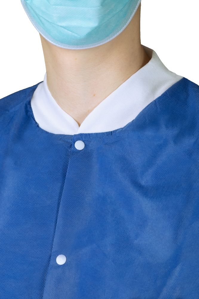 Nahaufnahme der Medi-Inn Wärmejacke für OP, Station und Pflege, langarm, blau – Zeigt den oberen Bereich mit weißen Druckknöpfen, weichem weißen Kragen und feinem Vliesstoff, getragen von einer Person mit OP-Maske.