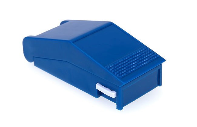 Ein Pillenschneider steht zentral im Bild, aus Kunststoff in Weiß und Blau. Der Schneider hat eine klare Klinge zum einfachen Zerteilen von Tabletten. An der oberen Seite befindet sich ein gelber Druckknopf, der zum Öffnen des Geräts dient. Der Boden zeigt eine rutschfeste Beschichtung, um Stabilität zu gewährleisten. Der Hintergrund ist neutral und hell, was den Fokus auf den Pillenschneider legt.